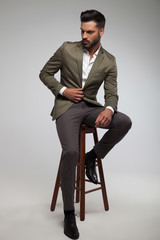 attractive man in green suit sits on wood stool