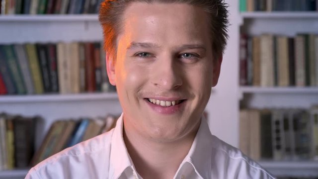 Young man is watching at camera, smiling, making eyes, flirt concept, blurred background