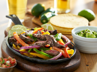 mexican beef fajitas in iron skillet with guacamole and beer