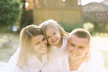 portrait of smiling family with little daughter resting on cloth on ground together on backyard