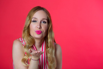beautiful young woman in a bright shirt on a red background sends an air kiss