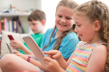 Obraz premium Three Children On Sofa At Home Playing With Digital Devices