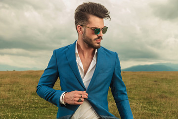 attractive smart casual man with sunglasses buttoning blue suit outside