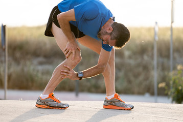 runner holding his knee in pain after pulling a muscle.