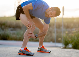 runner holding his knee in pain after pulling a muscle.