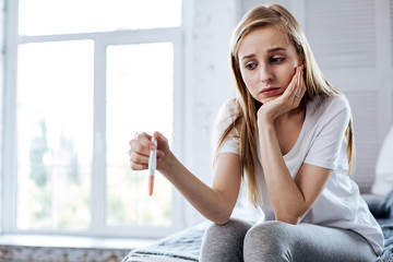 Fototapeta premium Bad mood. Unhappy young woman sitting and holding her pregnancy test