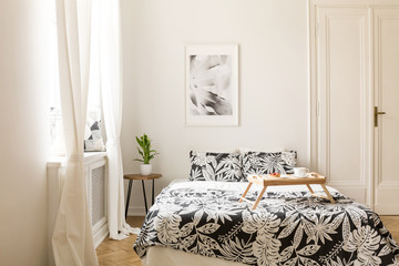 Real photo of a double bed with patterned sheets and wooden breakfast tray in a white bedroom...