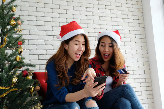 Two young cute asia women holding smartphone and credit card while shopping online with happiness, Christmas holiday shopping concept