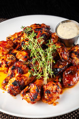 Mexican cuisine, fried chicken wings in glazed hot sauce with thyme on a white plate with tartar...
