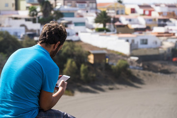 man from backside using cellular phone with internet connection and app. old town and beach in the background. summer time and leisure activity relaxing
