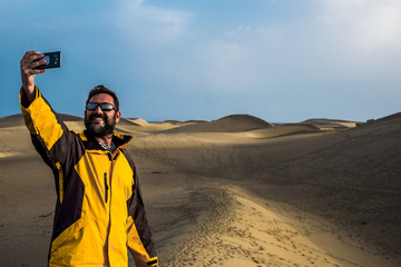 man traveler take a selfie picture using the smartphone with a desert and ocean in background. adventure and alternative vacation concept for caucasian people. enjoy life and freedom and nature