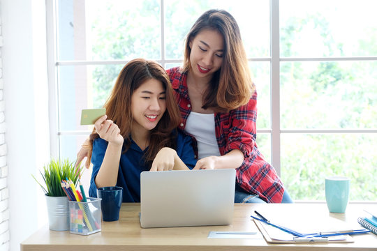 Two young asian women holding credit card and using laptop computer for shopping on line at cafe, business and technology concept, digital marketing, casual lifestyle