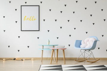 Poster mockup on the wall with triangles wallpaper in bright kid's room interior with pastel furniture and a knot cushion on a rocking chair. Real photo
