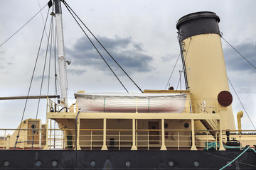 Close up fragment of old retro ship with lifeboat and funnel on sky background