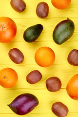 Fresh fruits background, top view. Variety of fresh organic fruits including oranges, kiwi fruits, mango, grapefruits and avocado on yellow wooden background. Healthy food and diet.