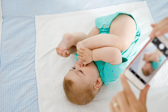 Parent taking photo of a baby with smartphone. Adorable newborn child taking foot in mouth