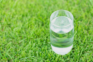 Closeup glass of water on green grass nature background, food healthy concept