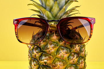 Close up stylish sunglasses on pineapple. Fresh juicy pinapple in sunglasses on yellow background...