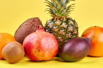 Assortment of tropical fruits on yellow background. Mix of colorful exotic fruits on color background, front view. Summer harvest of delicious fruits.