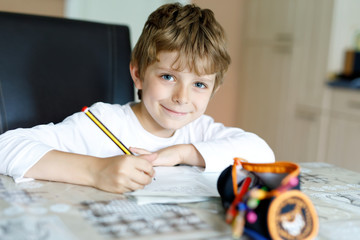 Tired kid boy at home making homework writing letters with colorful pens