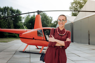 Helicopter flight. Cheerful glad woman crossing hands and standing near helicopter