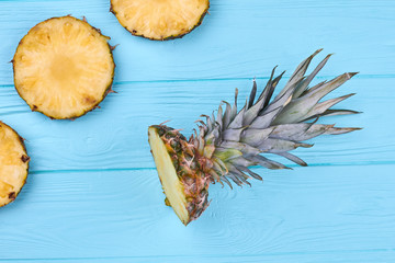 Freshly cut circle slices of pineapple. Flat lay pineapple crown on blue wooden surface. Healthy eatable plant.