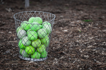 Old faded tennis balls piled up in metal wire basket placed on the ground with copy space