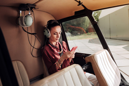 No rest. Attentive serious woman sitting in helicopter and texting on phone