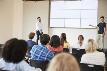 Male Student Giving Presentation To High School Class In Front Of Screen