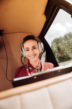 First time. Low angle of gay optimistic woman sitting in helicopter and smiling to camera