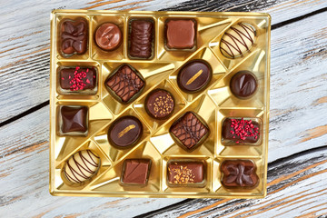 Assorted chocolate candies in golden box. Group of delicious chocolate pralines on wooden...