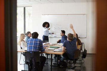 Female High School Tutor At Whiteboard Teaching Maths Class With Pupil Asking Question