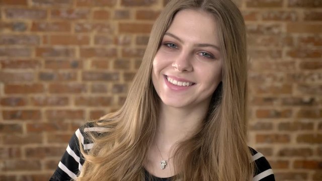 Young sweet blonda is watching at camera, smiling, dreaming concept, brick background