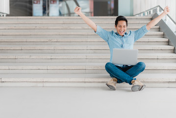 Excited Asian man raising arm up to celebrate success with laptop