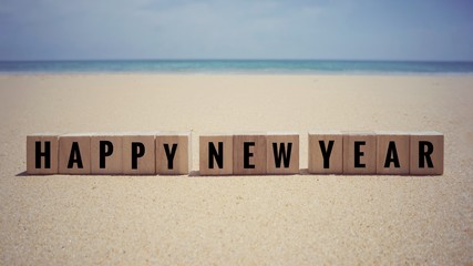 New Year Concept - ‘Happy New Year’ written on wooden blocks. With background of a beautiful beach.