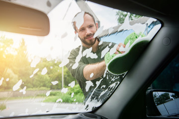 handsome man cleaning car front window with rag and soap at car wash
