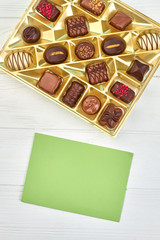 Box with chocolate candies and blank card. Set of chocolate candies on white background, top view. Beautiful present on Birthday.