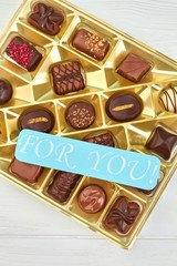Box of various chocolate candies, top view. Assortment of candies in opened box and message for you.