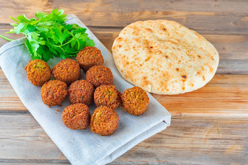 Falafel balls, pita and green fresh parsley on a wooden background, rustic style. Falafel is a...