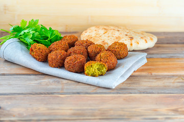 Falafel balls, pita and green fresh parsley on a wooden background, rustic style. Falafel is a traditional Middle Eastern food, commonly served in a pita.