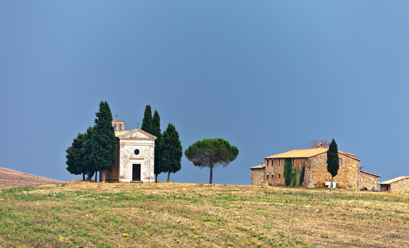Italy. Tuscany. Val d'Orcia. Pienza. Famous old Cappella della Madonna di Vitaleta 1590 and cypress trees on the hill against the background of the autumn blue sky