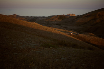 Amazing scenic view of mountainous area and sea in background with white car parked in valley. Travelers sleeping in tent on campsite during road trip, enjoying amazing landscape when nobody around