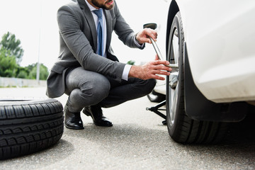cropped image of businessman changing tires on car on road © LIGHTFIELD STUDIOS