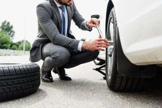cropped image of businessman changing tires on car on road