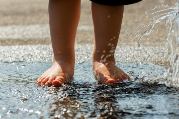Kleinkind planscht mit nackten Füßen in spritzender Wasserpfütze