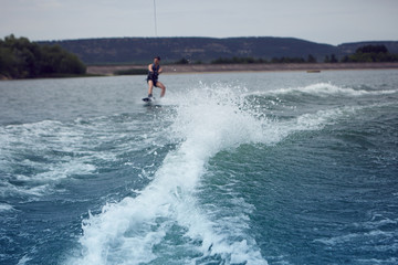 Attractive young male wakeboarder enjoying summertime watersports activity on river. Happy man in swimsuit wakeboarding outdoors towed behind motor boat. People, vacation and sports concept