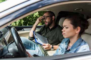 dissatisfied teacher touching forehead in car during driving test