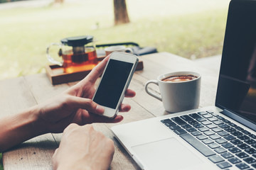 Business man holding phone and using laptop on wooden table. Vintage toned.
