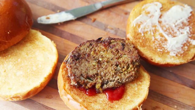 A woman puts meatloaf, pickles, lettuce and tomato on toasted brioche buns