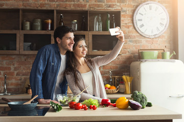 Happy couple cooking and taking selfie in kitchen